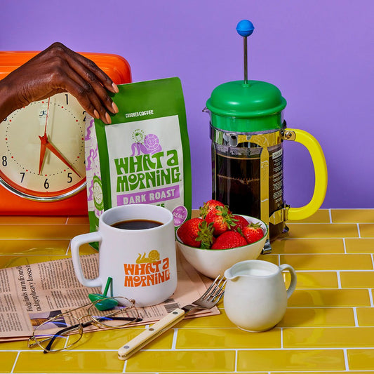 What a Morning Dark Roast Coffee surrounded by a What a Morning mug, and a French Press all in a kitchen scene