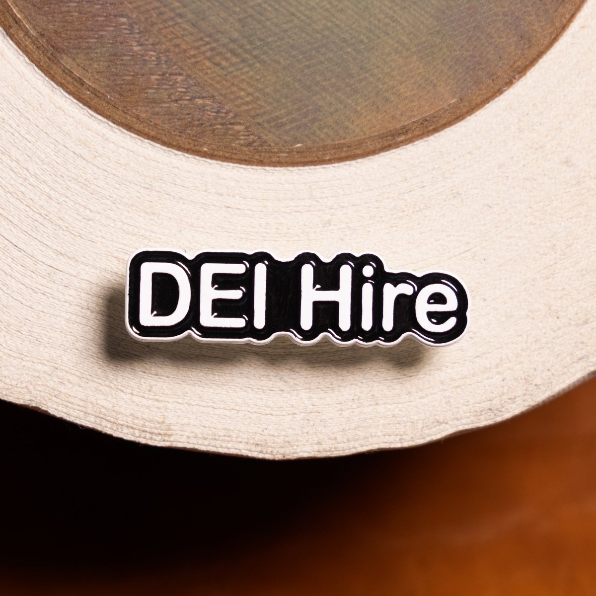 Pin with 'DEI Hire' text on a beige cap