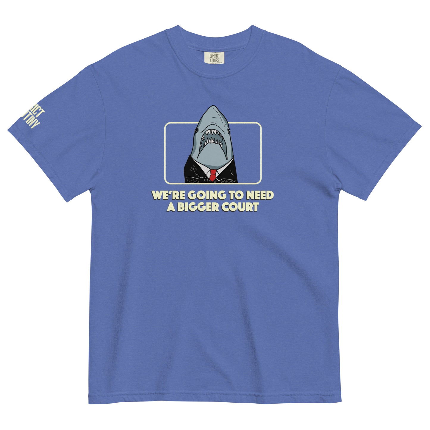 A blue short-sleeve t-shirt with a graphic of a shark dressed in a black suit and red tie, framed by a light yellow border, with the text 'WE'RE GOING TO NEED A BIGGER COURT' printed below. Strict Scrutiny logo in light yellow is visible on the left sleeve
