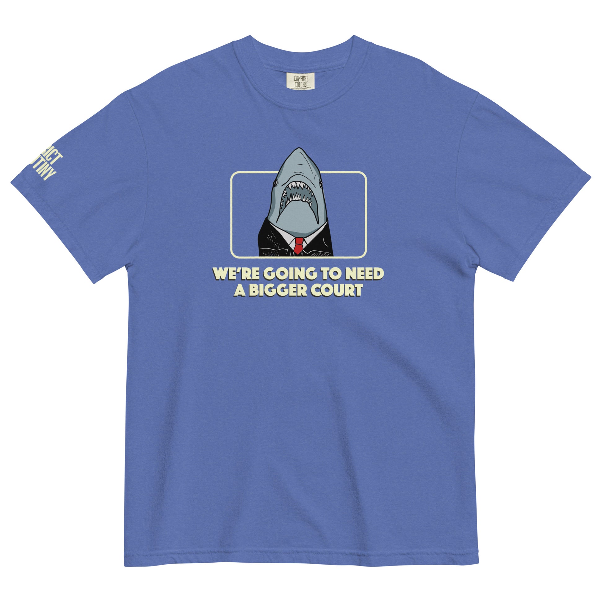 A blue short-sleeve t-shirt with a graphic of a shark dressed in a black suit and red tie, framed by a light yellow border, with the text 'WE'RE GOING TO NEED A BIGGER COURT' printed below. Strict Scrutiny logo in light yellow is visible on the left sleeve