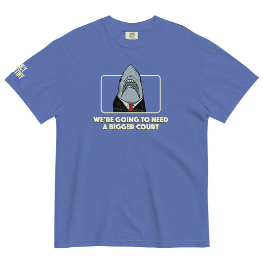 A blue short-sleeve t-shirt with a graphic of a shark dressed in a black suit and red tie, framed by a light yellow border, with the text 'WE'RE GOING TO NEED A BIGGER COURT' printed below. Strict Scrutiny logo in light yellow is visible on the left sleeve